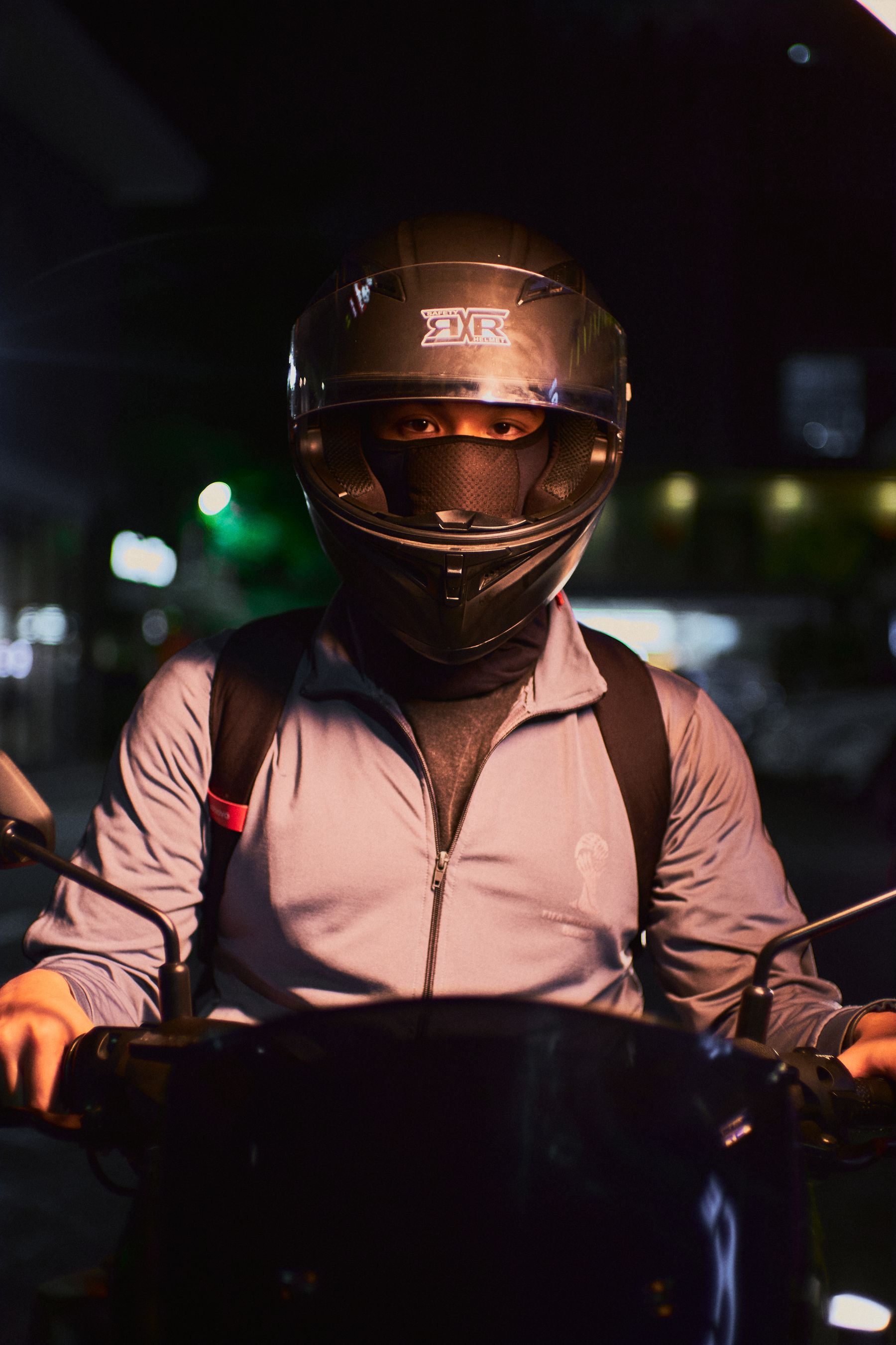Motorcycle rider wearing a full face helmet beside a motorcycle in an urban night environment