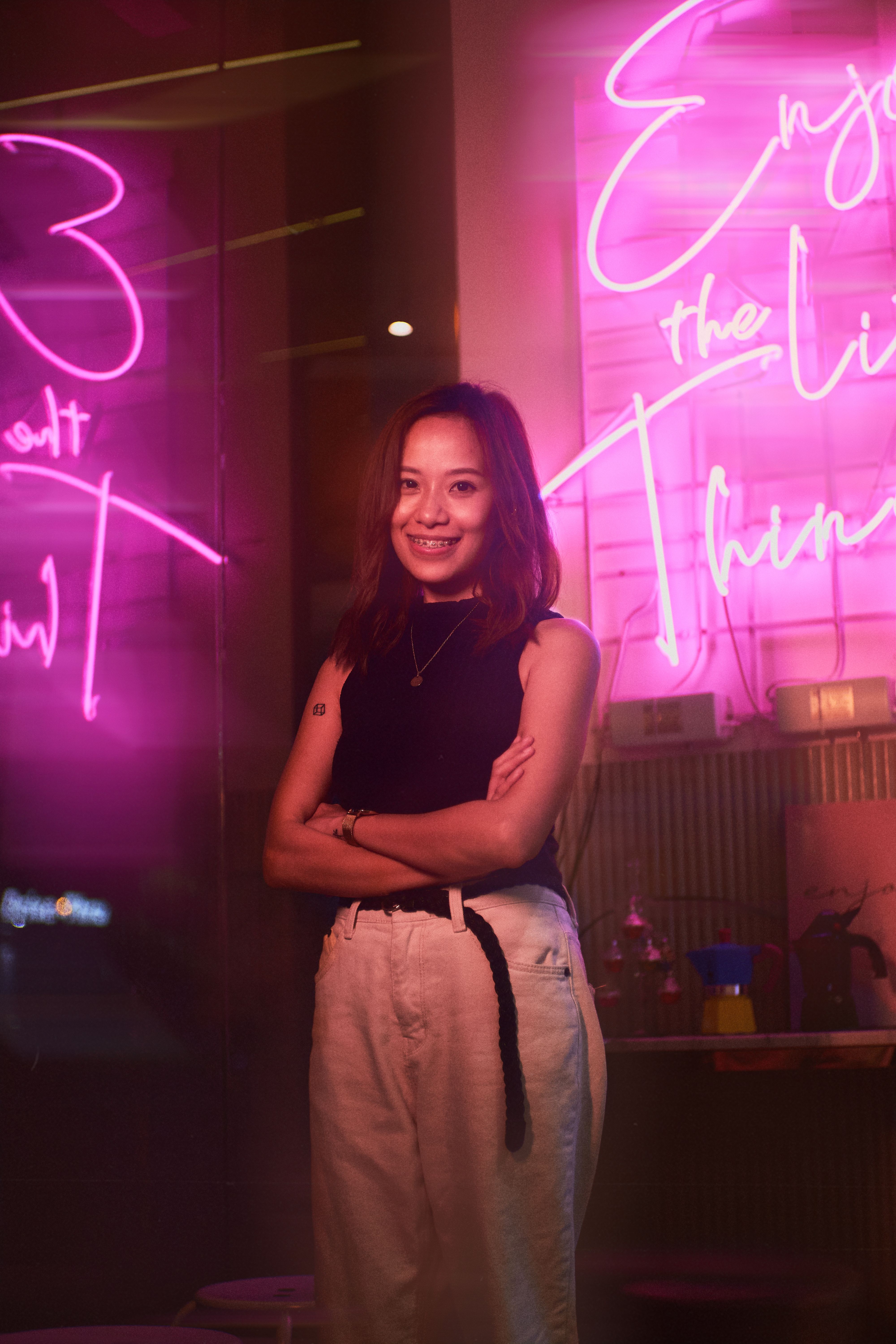 A woman stands confidently against a vibrant neon-lit background, exuding joy and style.
