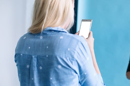 Blonde woman using a smartphone indoors. Back view showing leisure time.