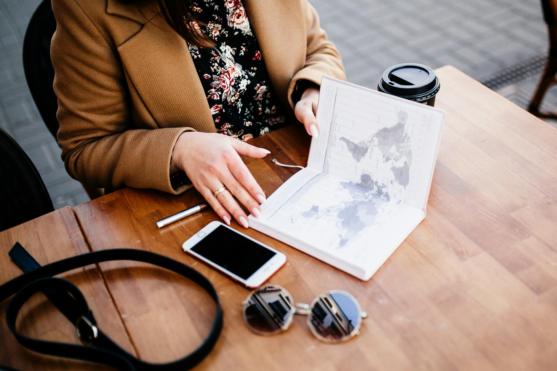 A woman views a travel planner and map on a wooden table, accompanied by coffee and a smartphone.