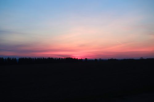 Free A tranquil countryside sunset with colorful sky and silhouette trees. Stock Photo