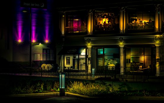 A vibrant restaurant exterior with colorful lights and people dining upstairs at night.