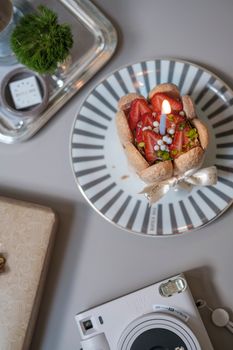 Close-up of a decorative strawberry cake with a lit candle on a stylish plate, perfect for celebrations.
