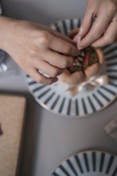Close-up of hands decorating a dessert with nuts on a stylish plate, creating a chic presentation.