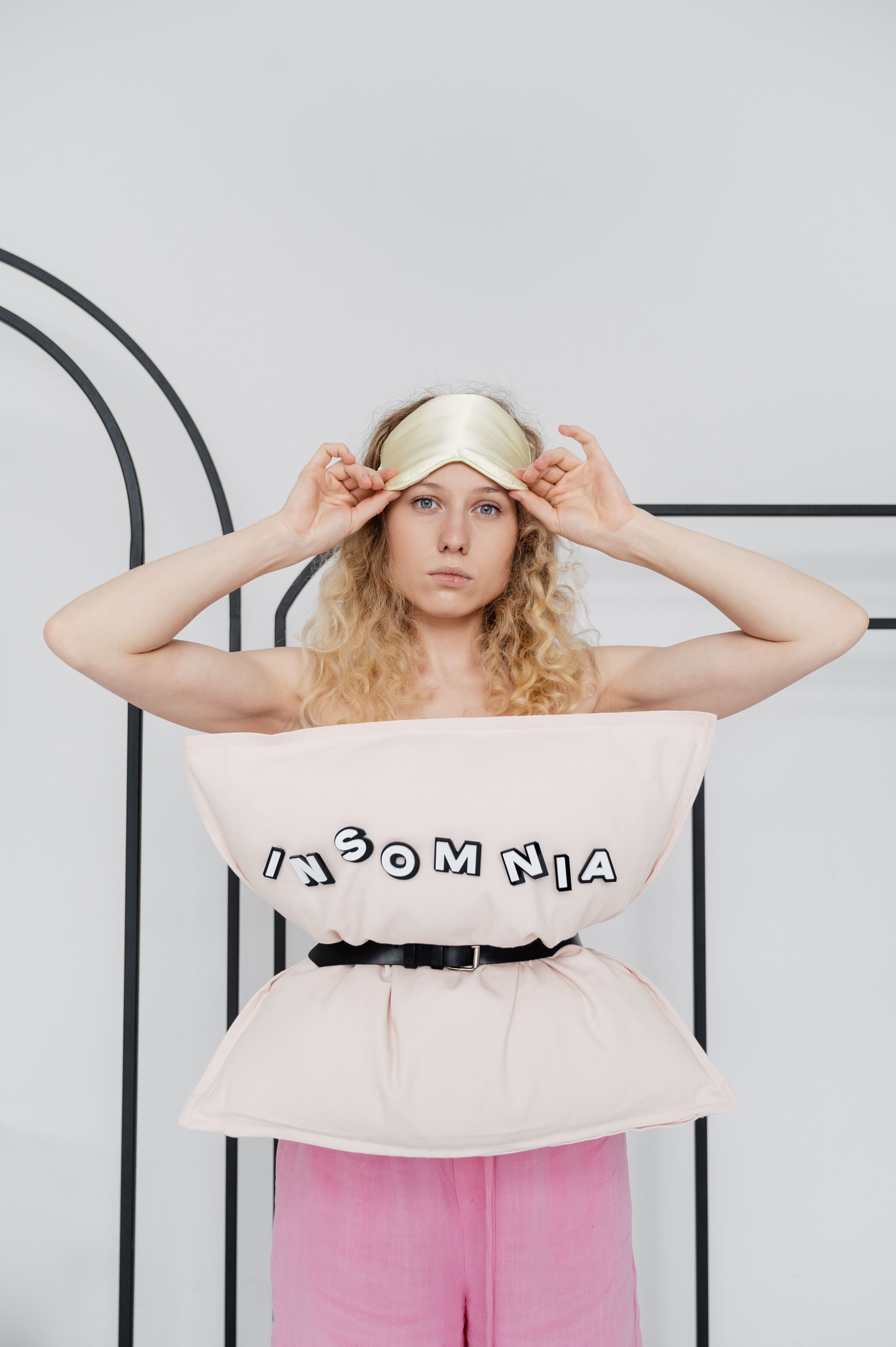 A creative portrayal of insomnia with a woman wearing a pillow outfit, holding a sleep mask.