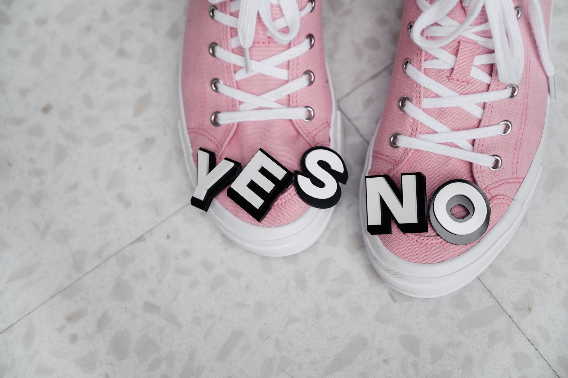 Pink sneakers with YES and NO letters on a tiled floor, symbolizing choice.