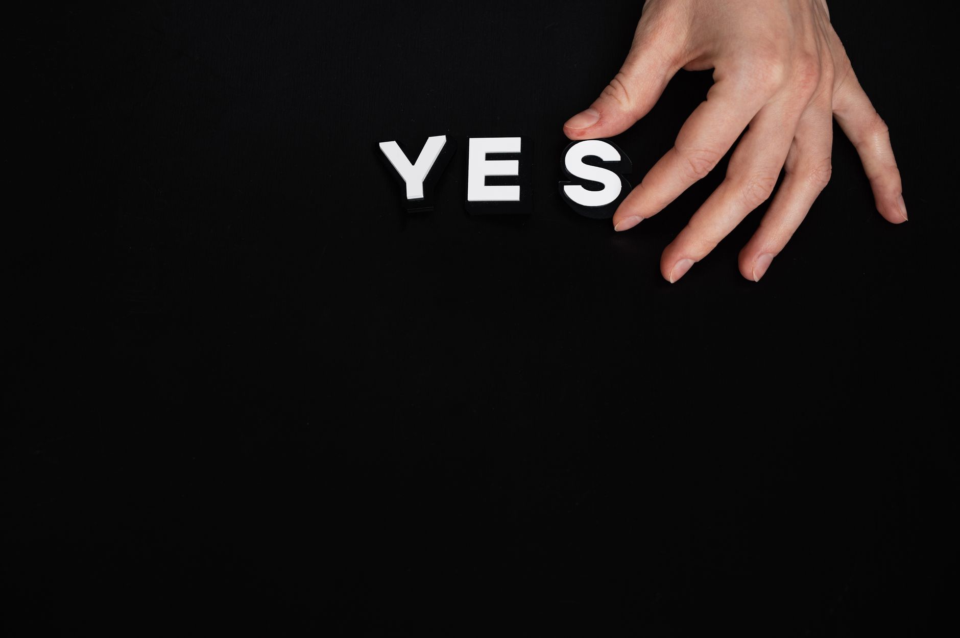 Hand arranging the word "YES" with white letters on a black background.