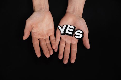 Free Hands presenting the word 'YES' against a black background, symbolizing positivity and agreement. Stock Photo