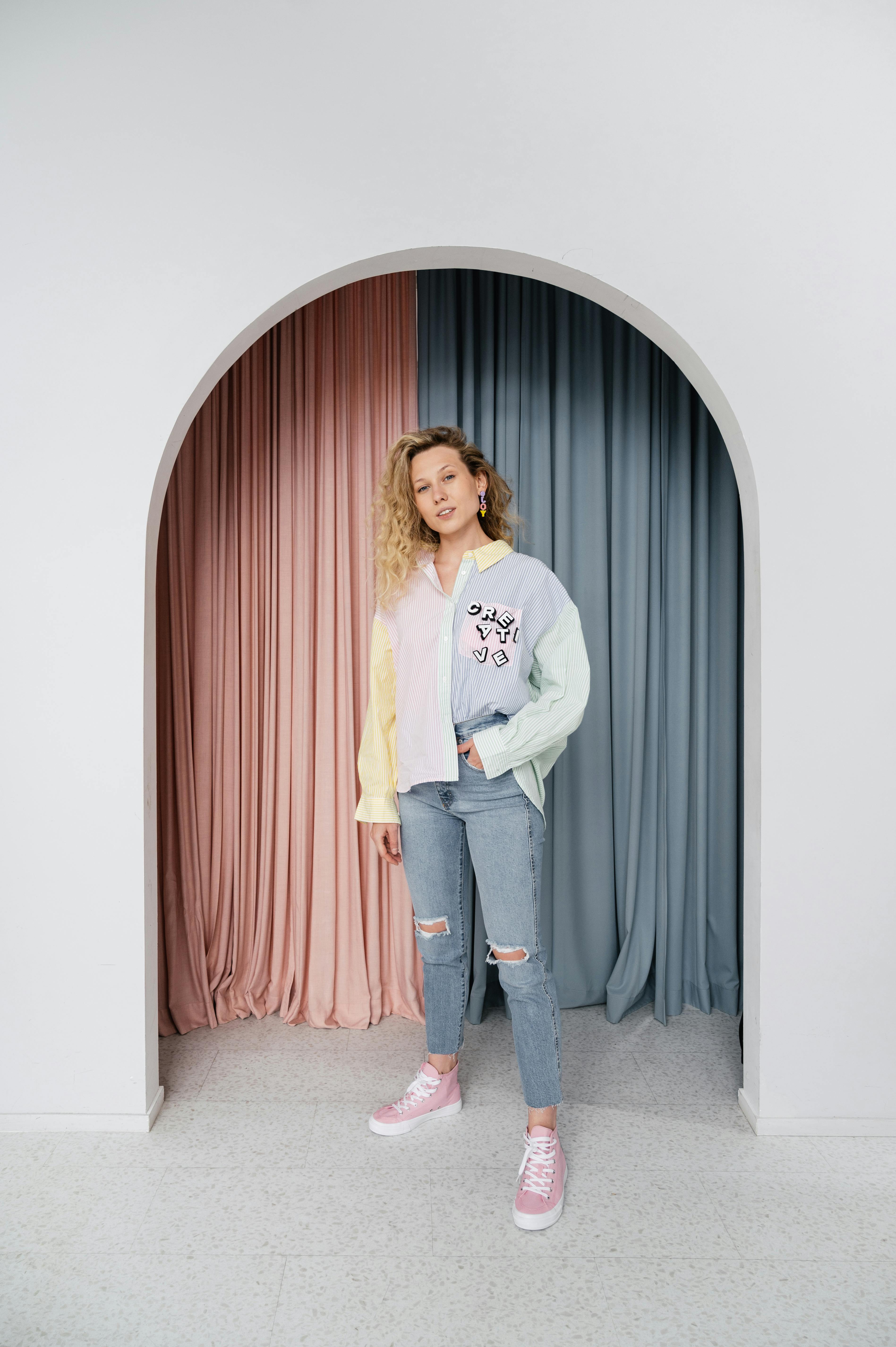 Fashionable woman in pastel outfit posing against colorful curtains indoors.