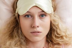 Blonde woman wearing a sleep mask, looking awake and worried, highlighting insomnia.