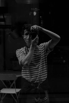Monochrome photo of a masked photographer in a reflection, capturing the moment.