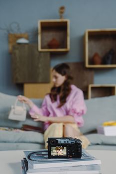 A woman in a pastel setting is reviewing a handbag on camera, showcasing lifestyle content.