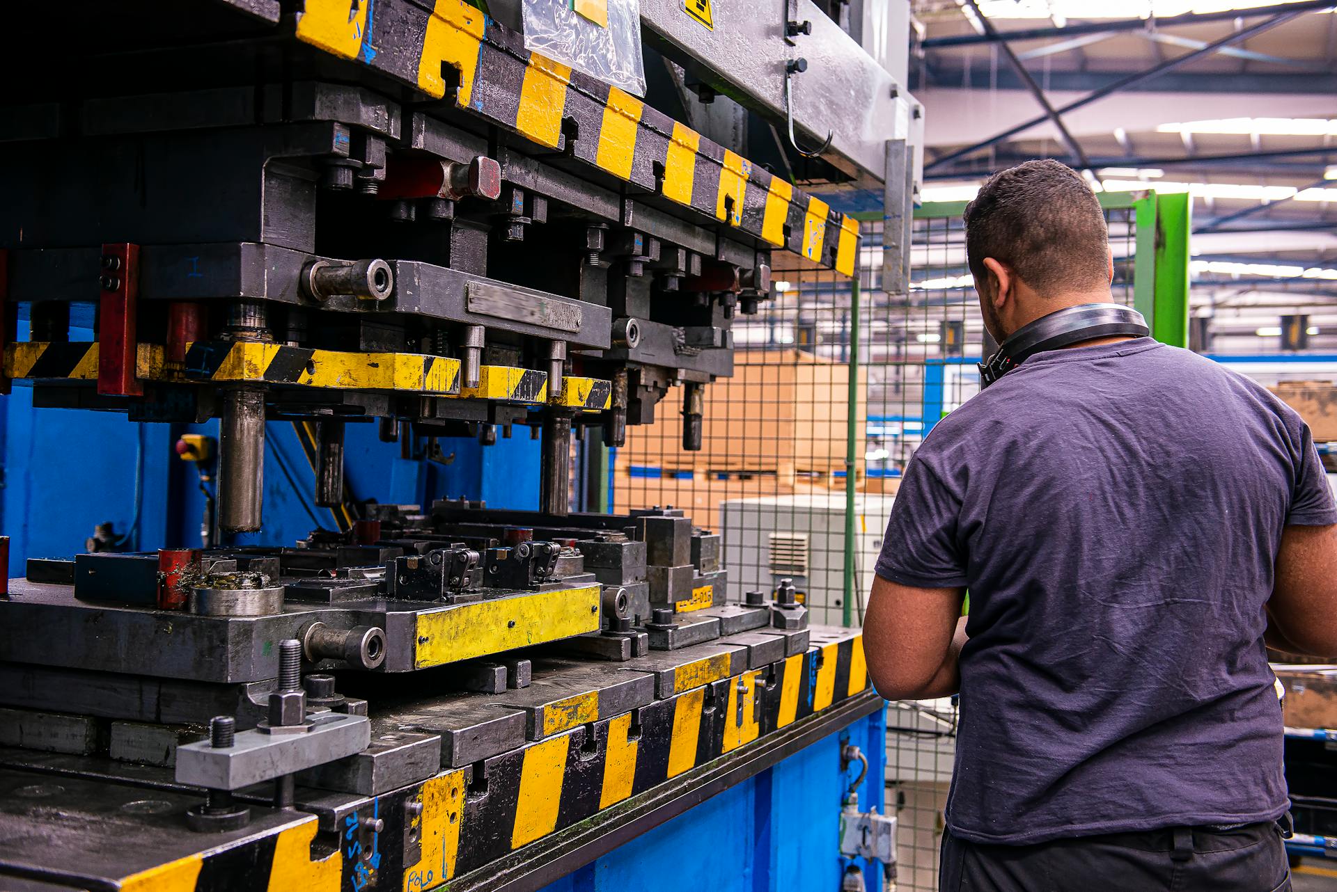 A back view of an adult male operating heavy industrial machinery in a factory setting.