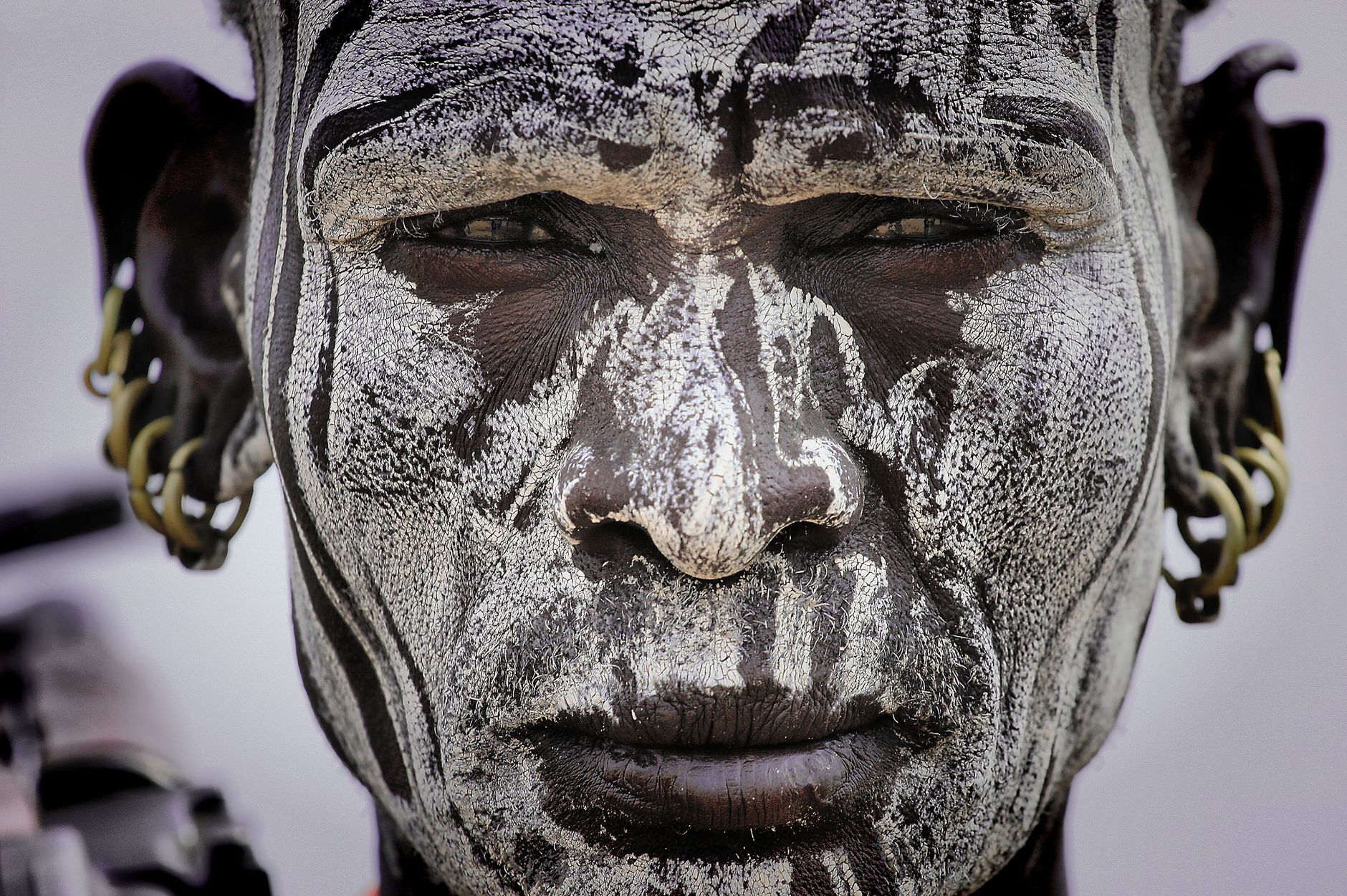 Close-up portrait of a person with tribal face paint and traditional earrings, showcasing cultural expression.