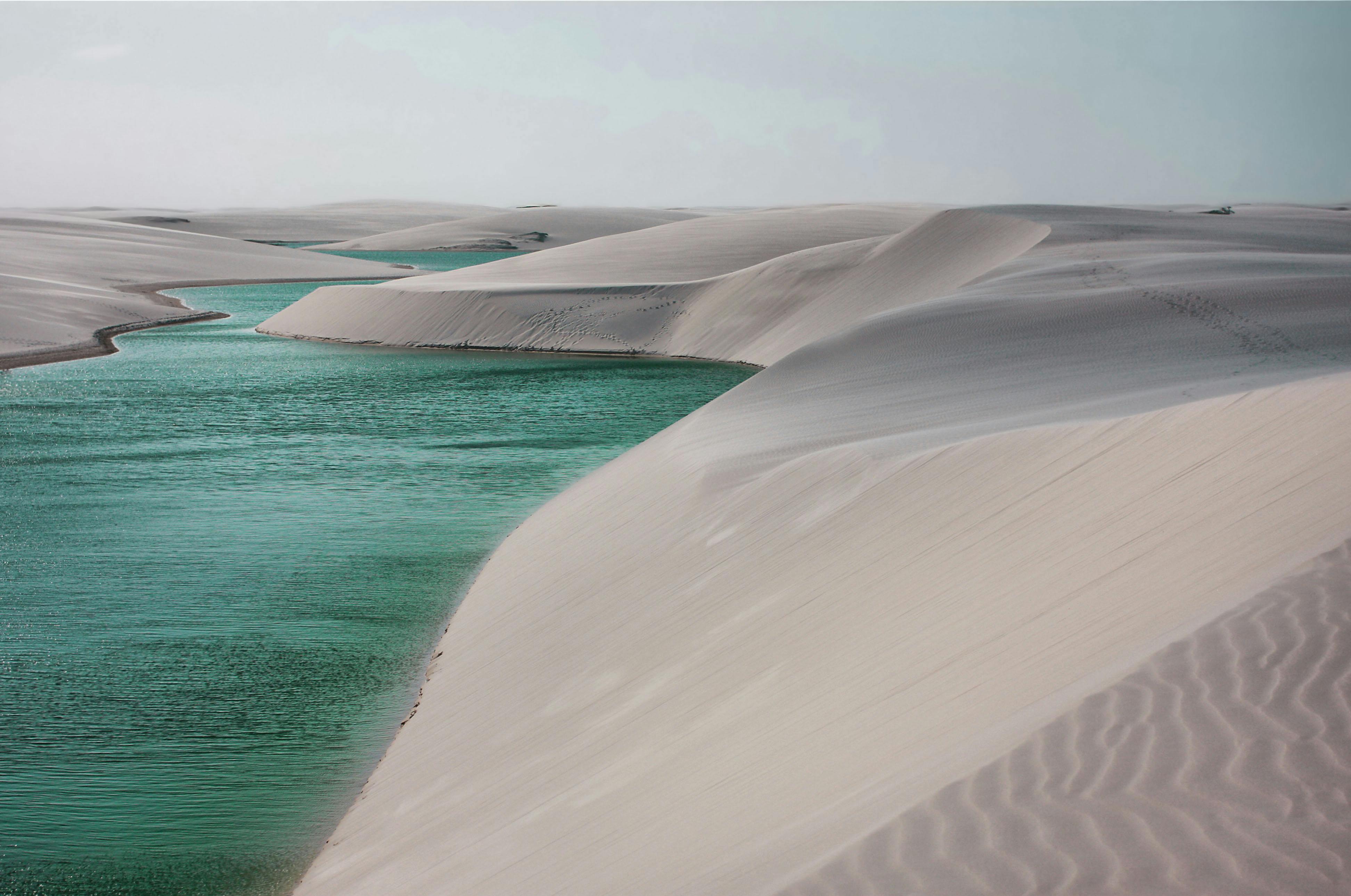 A picturesque landscape of rolling desert dunes with vibrant turquoise waters flowing through.