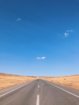 Straight road leading through barren landscape under a vivid blue sky in Kayseri, Türkiye.