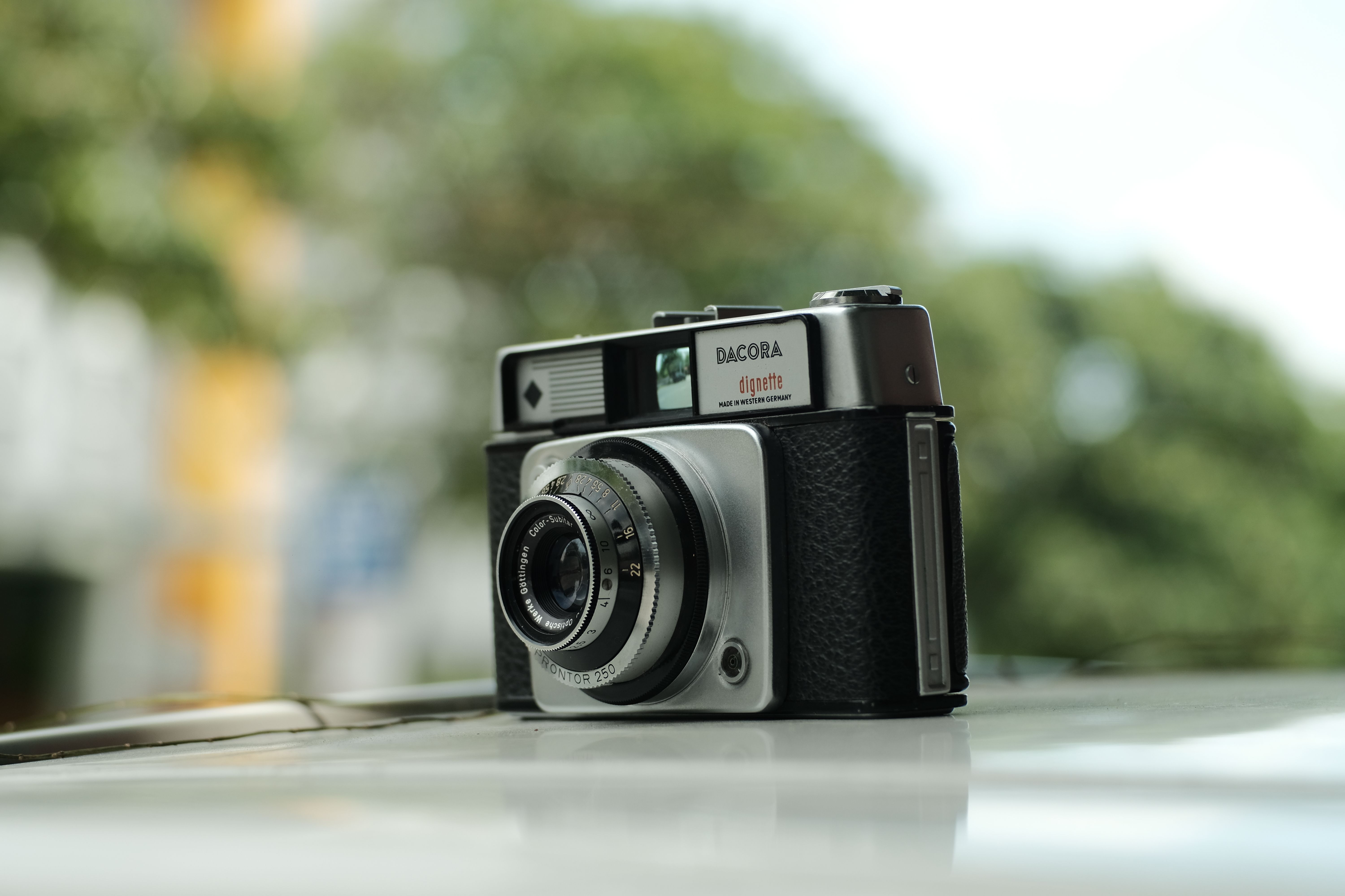 Close-up of a vintage Dacora dignette camera on a reflective surface outdoors.