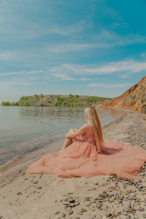 
A Woman Wearing a Pink Dress Sitting on the Beach