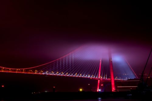 Free Suspension bridge beautifully illuminated in vibrant colors at night amidst a foggy atmosphere. Stock Photo