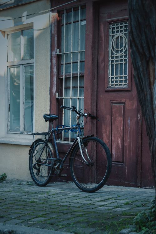 Free Rustic bicycle parked against a weathered door on a cobblestone street, evoking nostalgia. Stock Photo