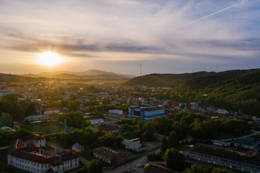 A breathtaking aerial view of an urban area with lush greenery and mountains at sunrise.