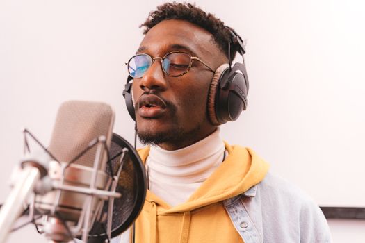 African American musician singing passionately in recording studio with headphones and microphone.
