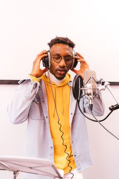Young man recording a music track in a studio wearing fashionable attire and headphones.