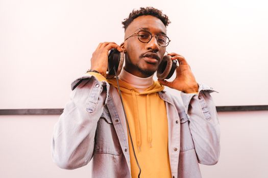 Young man in a denim jacket enjoying music with headphones indoors.