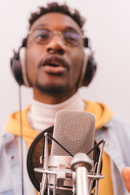 Close-up of a man singing into a microphone, wearing headphones indoors.
