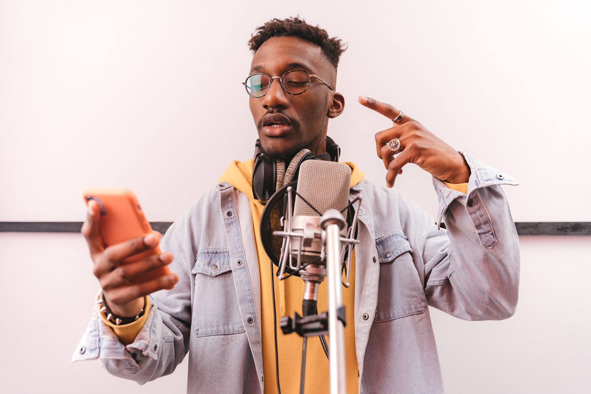 手機高音質錄音與樂曲備份實用指南 An adult male singer recording in a music studio with a smartphone and microphone.
