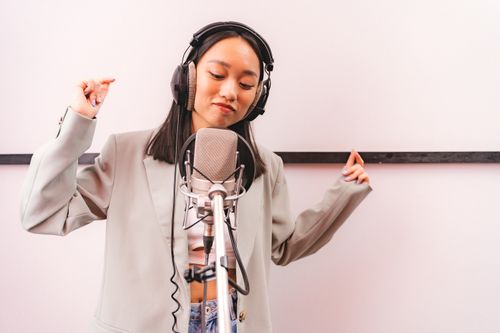 Free Asian woman singing in recording studio with microphone and headphones, expressing creativity. Stock Photo