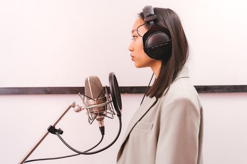 Free Side view of an Asian woman with headphones singing into a condenser microphone in a studio. Stock Photo