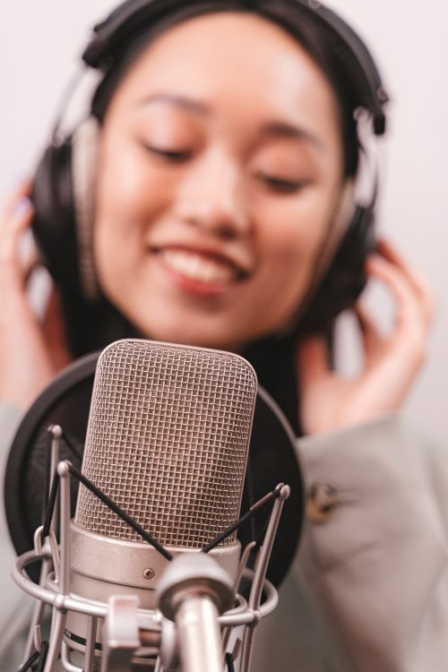 Free An Asian woman in a recording studio singing into a condenser microphone, wearing headphones. Stock Photo