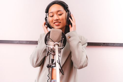 Free A female singer joyfully records vocals with condenser microphone in a music studio. Stock Photo