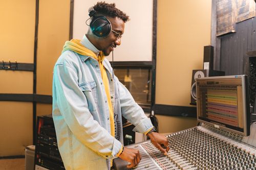 Free African American man using audio mixer in music studio wearing headphones and denim jacket. Stock Photo
