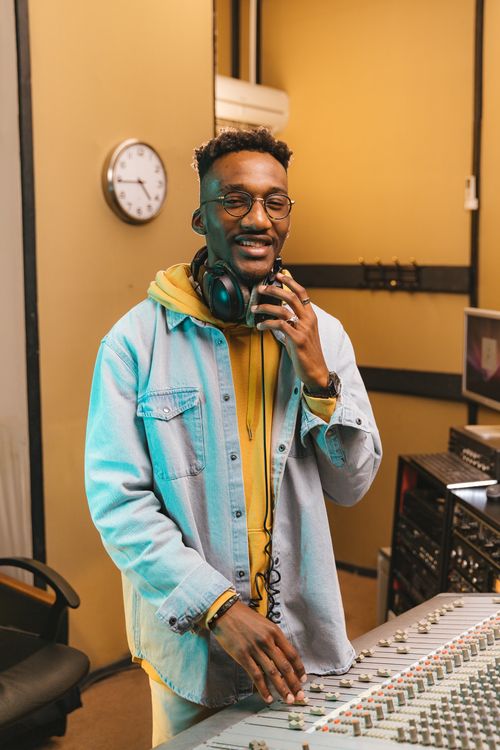 Free Smiling young man with headphones and denim jacket in a professional recording studio. Stock Photo