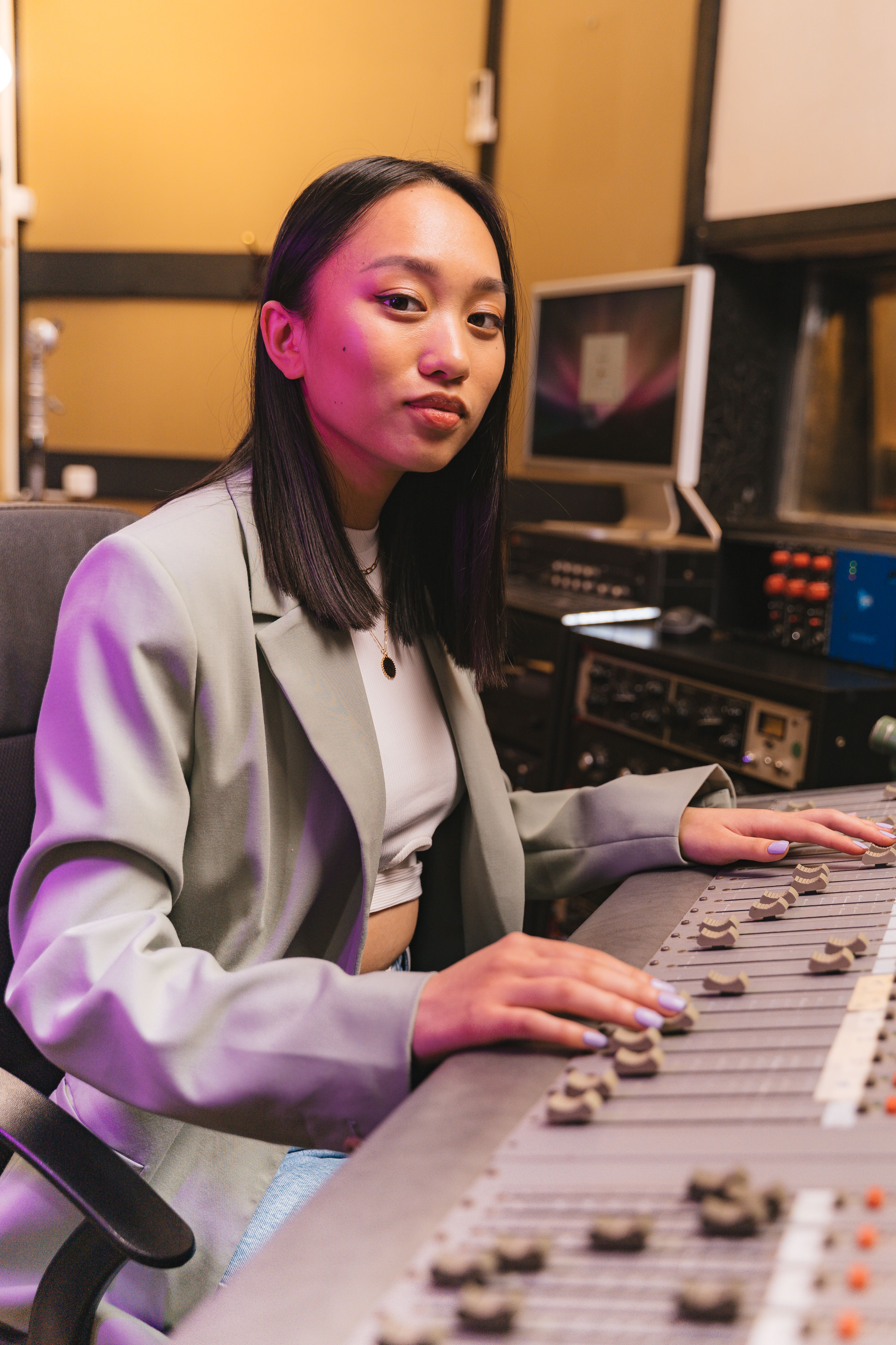 An Asian woman operates an audio mixer in a modern recording studio.