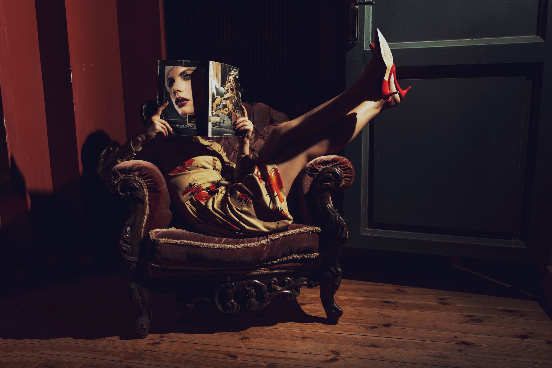 Woman in high heels reading a magazine while sitting in a vintage chair, creating a chic and stylish vibe.