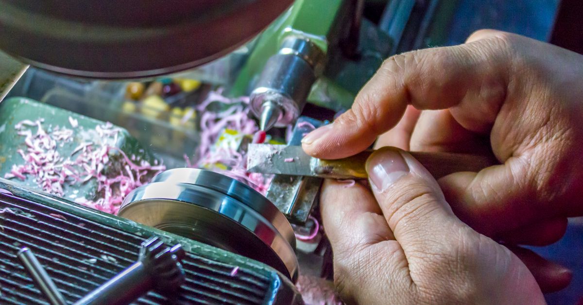 Hands carefully operate a metal lathe machine, showcasing precision in metalworking.