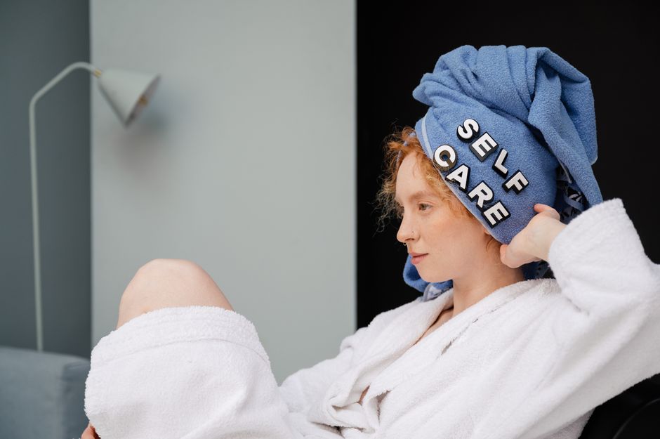 Como Cultivar a Autoconfiança com Práticas Diárias de Autocuidado 2 Relaxed woman in a bathrobe with a towel headwrap featuring 'self care' letters enjoying a moment at home.