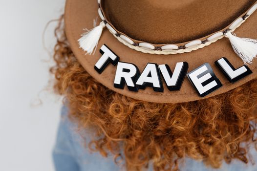 Close-up of a hat with 'TRAVEL' letters and red curly hair, perfect for travel-themed imagery.