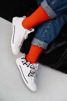Close-up of trendy white sneakers with 'TRAVEL' letters and orange socks for a modern style.