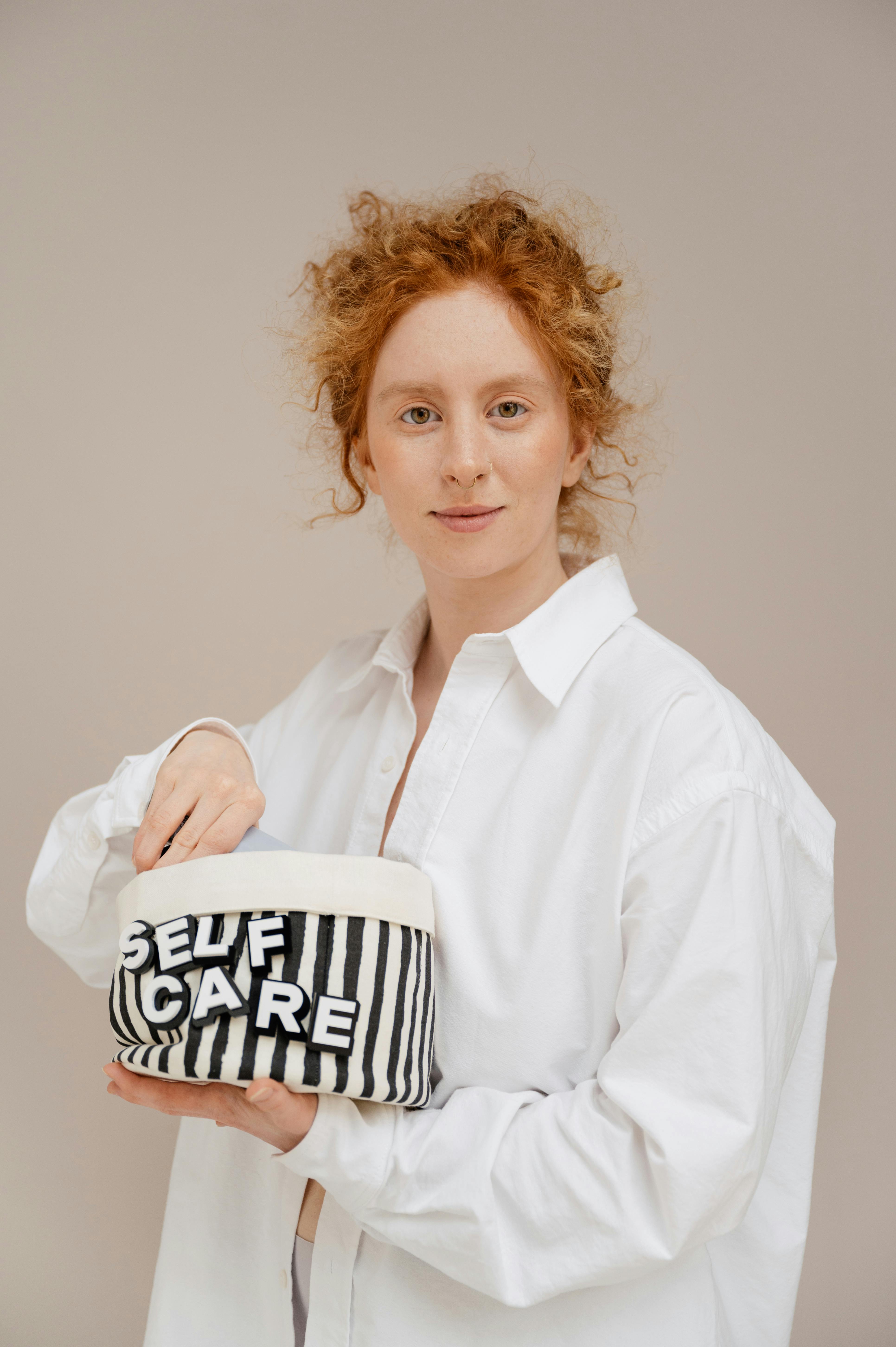A woman with red hair holding a bag labeled 'Self Care', emphasizing wellness.