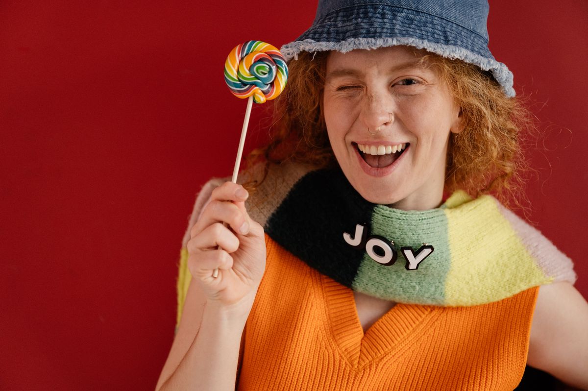 Woman in a colorful outfit holding a lollipop, embodying joy and happiness.