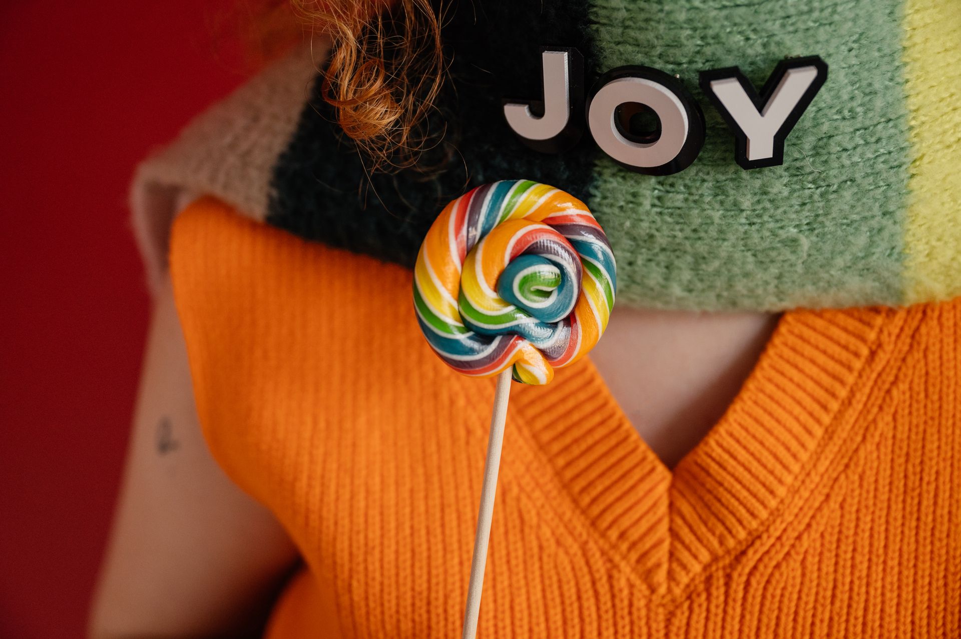 Close-up of a vibrant lollipop and 'JOY' text on a cozy scarf, evoking happiness.