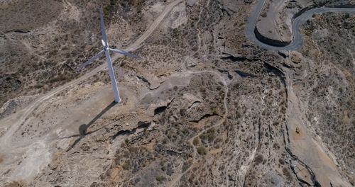 Free Drone shot capturing a lone wind turbine amidst rocky barren landscape with winding road. Stock Photo