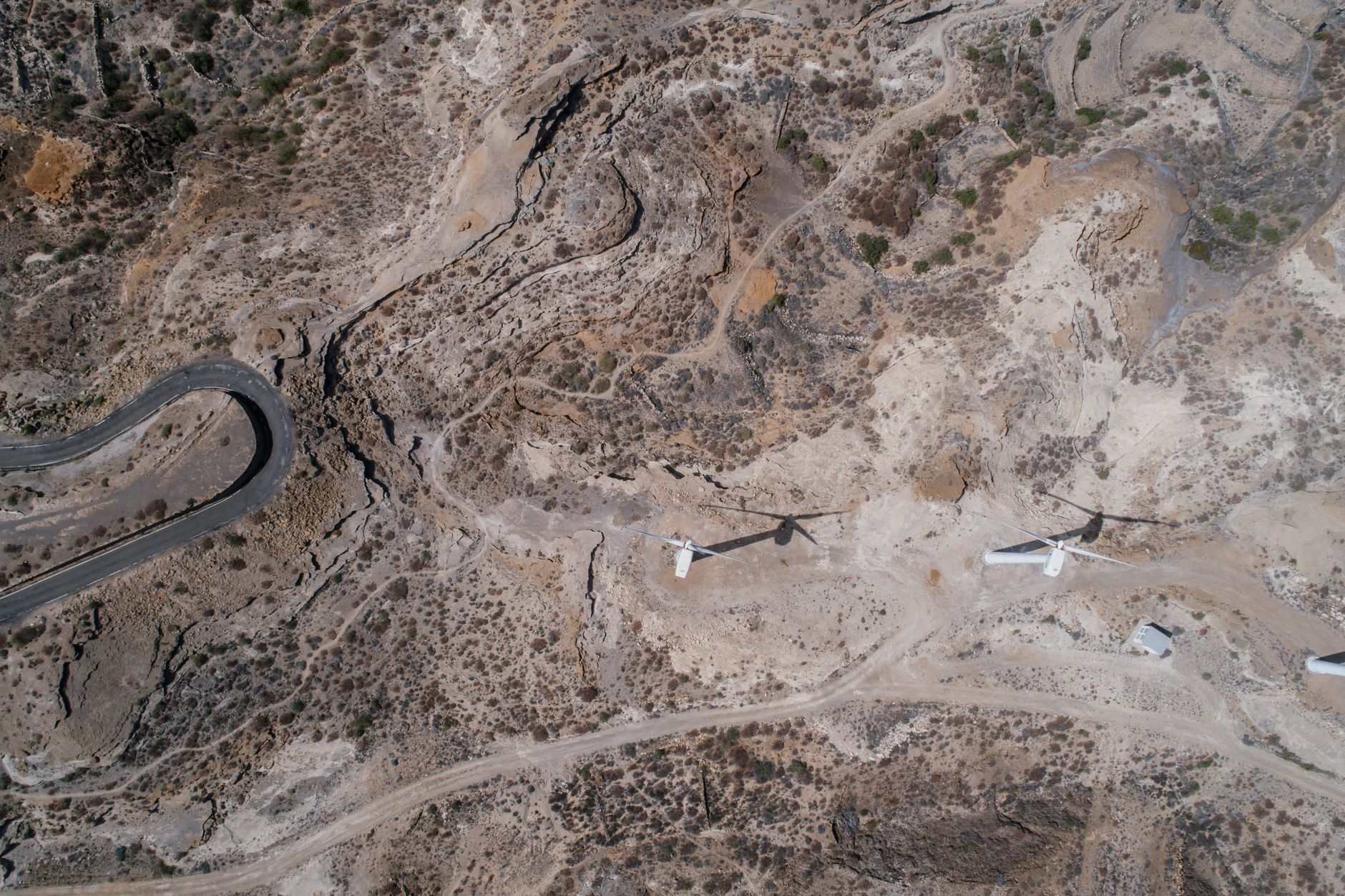 Drone shot of wind turbines in a dry, arid terrain with winding roads.