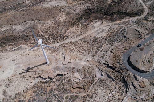 Free Drone shot capturing a wind turbine amidst a rugged desert landscape, showcasing sustainable energy. Stock Photo