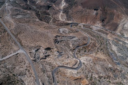Free Drone shot of a winding road through barren, rugged terrain. Stock Photo