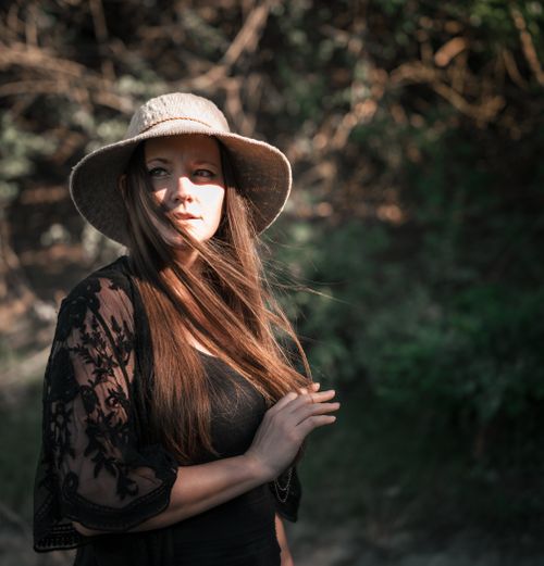 Free Woman with long hair and sun hat poses in natural outdoor setting with sunlight casting shadows. Stock Photo